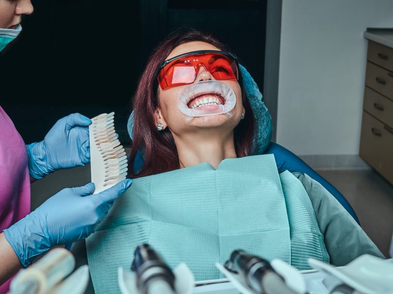 A woman dentist checks the level of teeth whitening with a dentist's color in the dentist office.